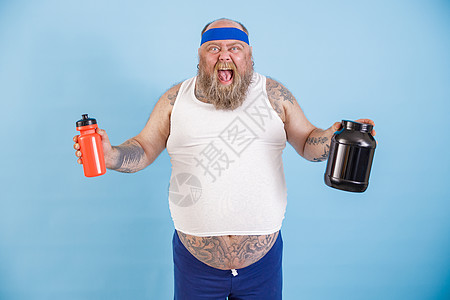 带头带的兴奋性大胖子 在演播室里拿着一瓶饮料和蛋白质补充品图片