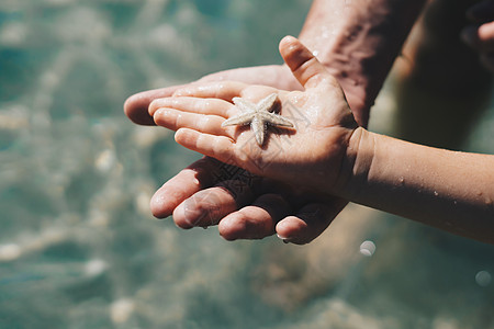 父亲握着儿子的手 儿童节目海星躺在张开的手掌上 特写湿滴皮肤 拇指手指 海上旅游 关心海洋动物自然世界的美丽 男孩的好奇心 一起图片