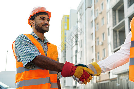 两名身穿工作服的工程师握手反对建筑工地建设者微笑男人人士施工技术男性工作背心经理图片