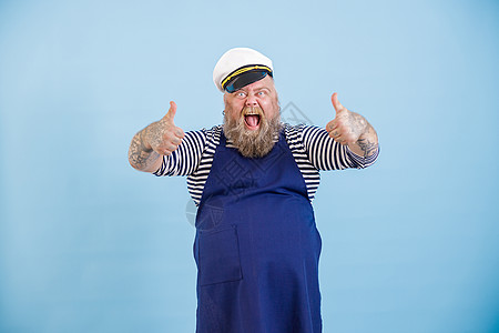 身穿水手西装超重男性情绪型男子 在浅蓝背景上露出大拇指图片