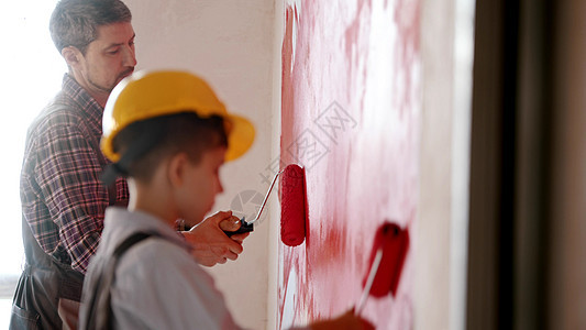 一个小男孩和他的父亲用红色粉刷墙壁 — 一个戴着头盔的男孩图片