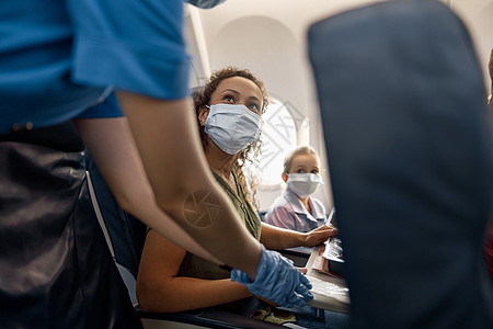 戴防护面罩的女人和她的小女儿看着女空姐帮助她们在飞机上调整和系紧安全带以确保旅行安全图片