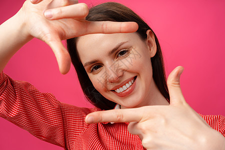微笑的年轻女子用手指对着粉红色背景展示一副表情图片