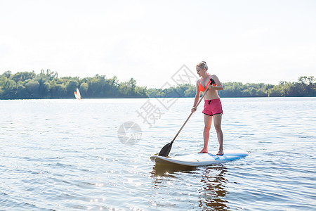 一个美丽的女人在阳光明媚的日子里 练习划桨太阳冲浪女孩桨板木板乐趣海滩平衡日落青少年图片