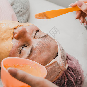 在美容院里用金面罩蒙着女人的脸 做手术花朵清洁沙龙油面膜粉末女士面具金子温泉治疗图片