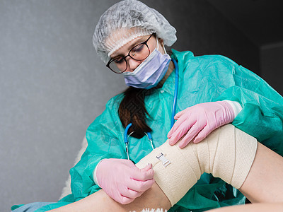 一名身戴医疗手套的年轻护士在病人的腿和膝盖上贴了弹性绷带 这是物理治疗室图片