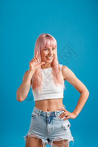 带着粉色头发的玩耍的年轻女人 笑着镜头 站在蓝工作室背景上图片