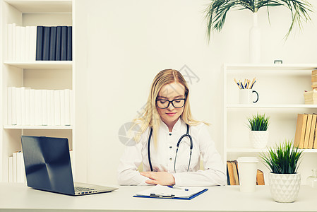 年轻美丽的女医生 在医院里快乐和微笑地工作 坐在桌子上护士外科房间卫生套装实验室访问手术诊所电脑图片