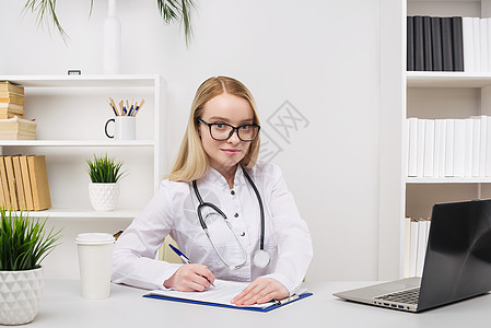 年轻美丽的女医生 在医院里快乐和微笑地工作 坐在桌子上套装保健从业者办公室科学卫生护士电脑手术访问图片