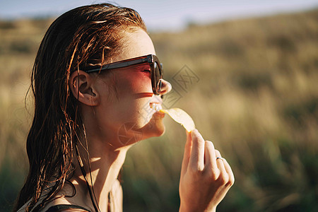 在自然阳光下吃薯片的太阳镜上筹码青少年乐趣成人芯片微笑饮食午餐垃圾女性图片