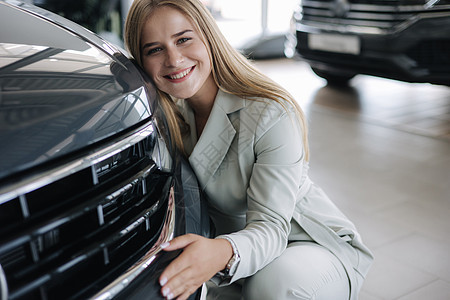 女商务人士在汽车展厅里选一辆新车 快乐的女士拥抱新车 很高兴经销商男性营业员推销员女性男人零售微笑车辆保险图片