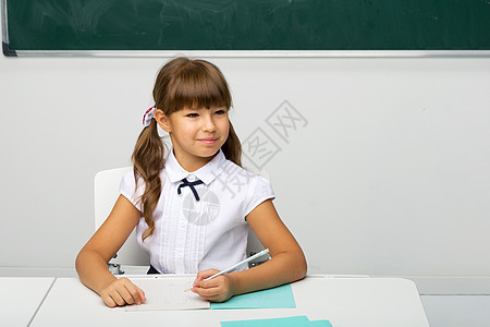 女孩在上课时坐在书桌边思考瞳孔桌子青少年童年黑板学生思维金发女性女郎图片