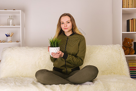 年青少女 脸长着膜的年轻女孩坐在沙发上 持有绿房子种植图片