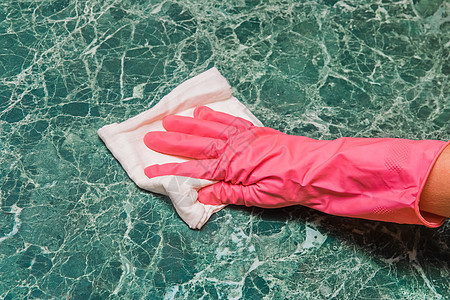 家庭主妇手握着粉红的家庭手套 在厨房用白布擦绿大理石表面图片