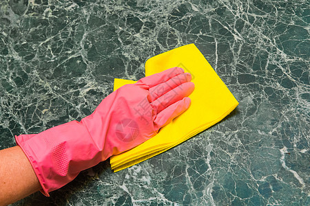 家庭主妇手握着粉红的家庭手套 在厨房用黄色布巾擦绿大理石表面图片