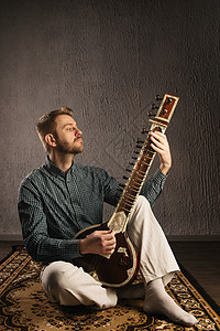 一位欧洲男子的肖像 他坐在地毯上玩西塔字符串喜悦成人娱乐音乐家吉他手乐趣乐器工作室闲暇图片
