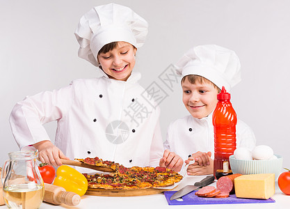 两个小厨师 分吃熟比萨饼香肠帽子胡椒孩子们快乐女孩厨房烹饪面粉盘子图片