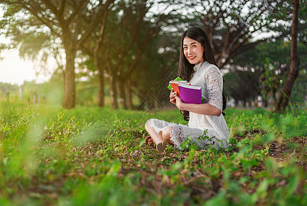 在公园持有一本书的年轻女子微笑学习裙子女性教育花园学生成人日落大学图片