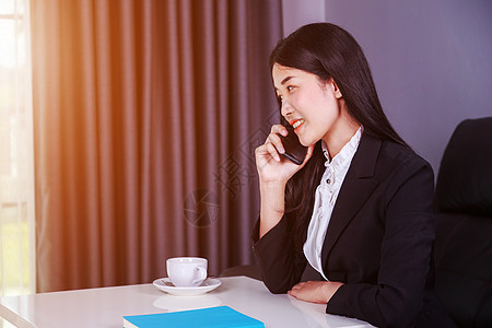 坐在办公桌边 在手机上聊天的开心女商业妇女杯子经理成人女性电话套装女士技术阳光办公室图片