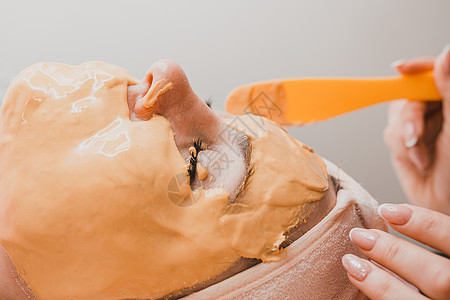 在美容学中使用金面罩 一名美容师妇女脸上戴金面罩女士温泉女性橙子美容奶油油面膜换肤沙龙治疗图片