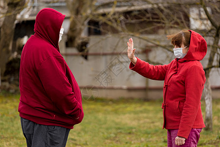 一位戴着防护性医用口罩的老妇人站在户外街道前 摆出手势 与一位老人保持社交距离图片