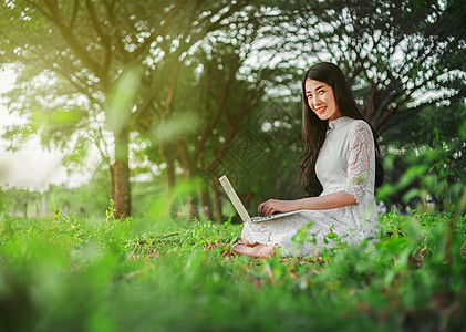 在公园使用笔记本电脑的美女技术商业阳光大学女性日落快乐学生花园教育图片