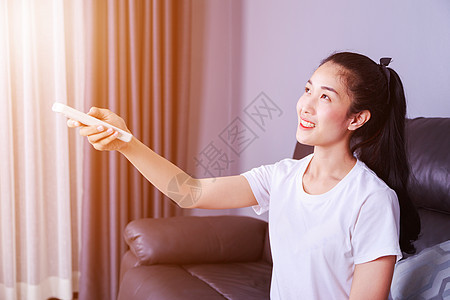 妇女在家沙发上用遥控空调机的沙发冷气机冷却器温度百叶窗女士力量女性状况成人阳光图片