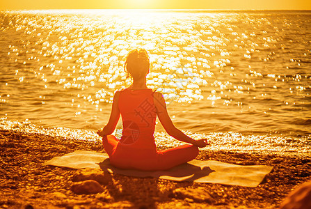 选择性的焦点 年轻漂亮的白人女子穿着红色西装 日出时分在海边的沙滩上练习瑜伽 瑜伽 健康的生活方式 冥想的概念套装身体平衡日落姿图片