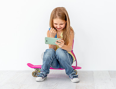 小女孩在看电话 坐在溜冰板上滑冰运动鞋童年溜冰者锻炼孩子们文化青年运动享受图片