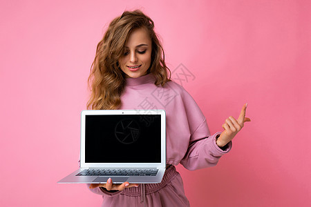 一张美丽的金发卷发年轻女性看着上网本键盘的照片 她拿着电脑笔记本电脑 上面有空的显示器屏幕 上面有模拟和复制空间 指着一根手指 图片