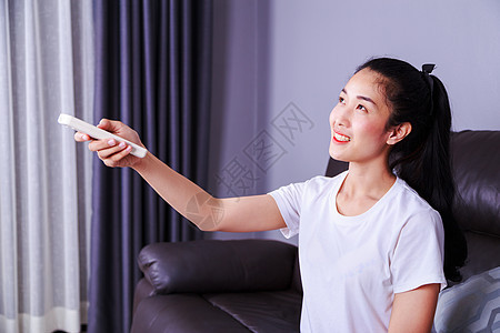 妇女在家沙发上用遥控空调机的沙发护发素百叶窗幸福控制微笑窗户女性房子力量女士图片