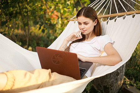 拥有笔记本电脑的妇女是吊床自由职业者旅行海滩上网女士互联网公园女性假期丛林工作女孩图片