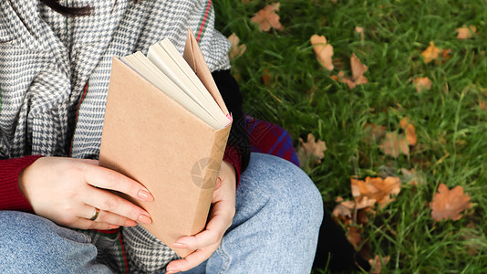 在秋天的公园里读书的女孩 在温暖的阳光明媚的日子里 女性的手在户外打开纸质书的页面 学生正在准备考试 文艺休闲自然文学森林手指寂背景图片