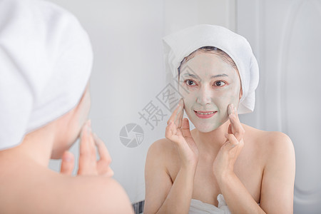 妇女脸上戴面罩 照镜子她们用面具遮着脸 看着镜子女士浴室治疗奶油温泉毛巾皮肤护理化妆品身体图片