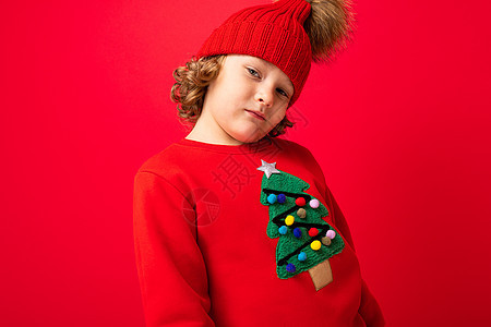 穿着温暖帽子和圣诞毛衣的金发美女男孩 红色背景 面带笑容男生孩子假期潮人派对微笑图片