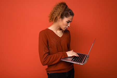 穿着红色毛衣 在红墙背景上被隔离的键盘上的网本显示器打字 校对背景图片