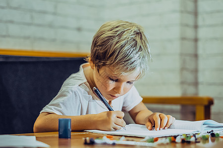 肖像金发可爱的学龄前男孩拿着笔笔记本看起来严肃认真勤奋努力学习写字 面部表情手势 儿童行为教育问题 家庭学校理念情感个性婴儿服装图片