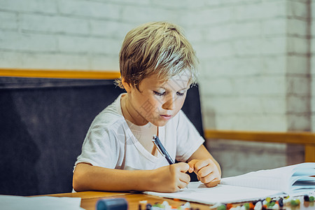 肖像金发可爱的学龄前男孩拿着笔笔记本看起来严肃认真勤奋努力学习写字 面部表情手势 儿童行为教育问题 家庭学校理念素描个性学生青年图片