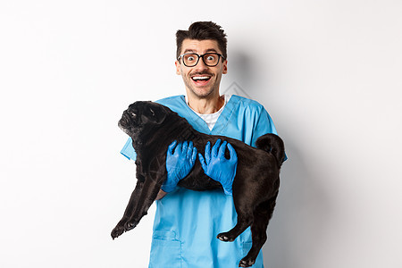 兽医诊所的概念 快乐的男医生兽医抱着可爱的黑哈巴狗 对着镜头微笑 白色背景宠物小狗动物犬类工作药品手套保健桌子成人图片