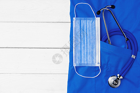 白色木质背景上带听诊器和面罩的医生医用制服诊所工具药品面具诊断疾病外科感染预防手术图片