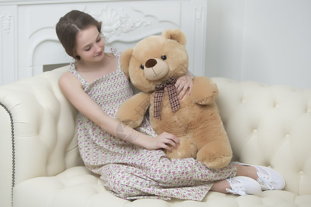 美丽的十几岁学龄少女坐在沙发上 带着泰迪熊坐着女性女儿长椅房间童年女士枕头喜悦父母微笑图片