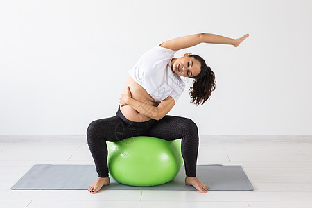 一名年轻孕妇坐在垫子上时使用健身球进行锻炼活动女性体操父母有氧运动瑜伽训练母性怀孕关爱肚子图片