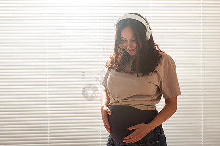 怀着卷发的快乐孕妇 在耳机里听音乐 复制空间腰部母亲女孩黑发怀孕唱歌腹部女性乐趣情绪图片