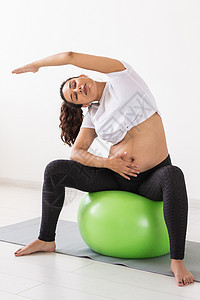 一名年轻孕妇坐在垫子上时使用健身球进行锻炼活动运动瑜伽母亲卫生肚子父母保健母性有氧运动训练图片