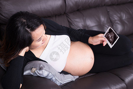 孕妇躺在沙发上 抱着孩子超声波照片肚子婴儿闲暇母亲保健女性怀孕房子休息成人图片
