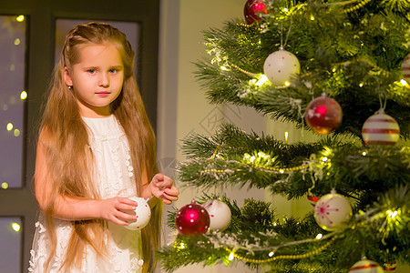穿着时尚服装的女孩坐在圣诞树前的地板上 笑声装饰品装饰庆典假期童年礼物幸福家庭针叶树针叶图片