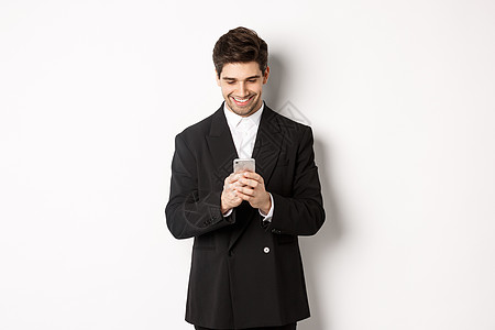 穿着黑西装的英俊时尚商务人士的肖像 写一个信息 微笑和看着智能手机 站在白色背景上标识套装经纪人商务广告男人金融购物横幅商业图片