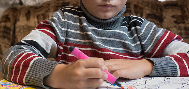 一个小男孩在家中的木制桌子上 画着彩色的蜡笔和毛笔图片