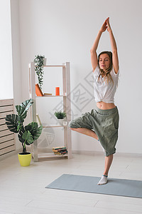 妇女从事瑜伽表演 在有植物和绿菜的舒适房间内垫子上套索 健康生活方式概念力量姿势沉思地面身体娱乐休息活动福利练习图片