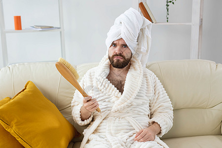 坐在沙发上的快乐男人的画像戴着头巾毛巾 手拿按摩刷 男性皮肤护理和水疗概念保健福利卫生身体沙龙胡子刷子乐趣喜悦微笑图片